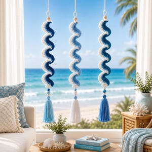 May include: Three vertical hanging decorations featuring a spiral wave design in shades of white, light blue, and dark blue. Each piece is suspended by a cord with a wooden bead and finished at the bottom with a matching yarn tassel and beads.