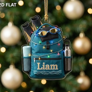 May include: A flat, teal-colored backpack ornament featuring the name Liam in gold lettering. The bag is adorned with a string of colorful Christmas lights, a pair of blue swimming goggles, a rolled-up towel, and a silver water bottle.