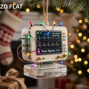 May include: A cream-colored medical monitor ornament featuring a screen with a heartbeat rhythm, SpO2 98%, HR 130 bpm, and the text Your Name. The device is wrapped in multicolored string lights, has gold knobs, and a base plate labeled EST. 2026.