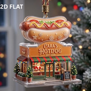 May include: A 2D flat hanging ornament shaped like a hot dog stand with a large hot dog on top. The sign reads Cara's Hotdog EST. 2026. The stand features a Santa figure inside, a customer outside, green and red striped awnings, and small trees.