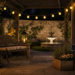 Peut inclure: Une guirlande lumineuse d'extérieur composée d'ampoules sphériques transparentes diffusant une lumière jaune chaude, suspendue sous une pergola en bois. Les ampoules sont espacées sur un fil sombre au-dessus d'une terrasse en pierre.