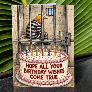 May include: A greeting card featuring a cartoon illustration of a person with blonde hair wearing a black and white striped prison uniform sitting in a jail cell behind bars. In the foreground, a white birthday cake with pink frosting and seven lit candles displays the red text: HOPE ALL YOUR BIRTHDAY WISHES COME TRUE.