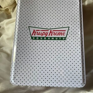 May include: White metal tin with a black polka dot pattern. The tin has a green and white Krispy Kreme Doughnuts logo.