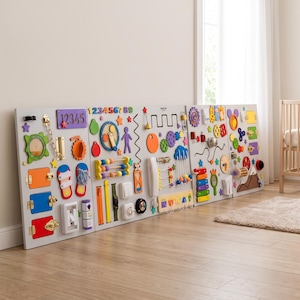Op de afbeelding: Een groot, meerdelig houten activiteitenbord met diverse sensorische elementen, waaronder kleurrijke tandwielen, grendels, sloten, telraamkralen, een telefoonhoorn, een xylofoon en cijferreeksen, gemonteerd op een lichtgrijze ondergrond.