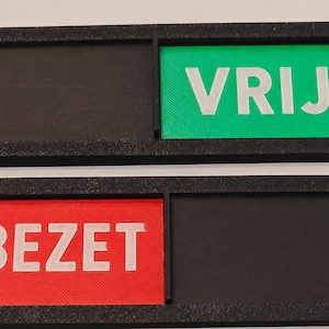 Könnte beinhalten: Zwei rechteckige schwarze Rahmen mit Schiebeelementen. Der obere Rahmen zeigt ein grünes Feld mit dem weißen Text VRIJ. Der untere Rahmen zeigt ein rotes Feld mit dem weißen Text BEZET. Jeder Rahmen verfügt über einen schwarzen Bereich.