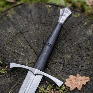Puede incluir: Una espada con hoja de acero pulido, una guarda recta y una empuñadura envuelta en cuero negro. El pomo tiene forma de diamante facetado, fabricado en acero pulido, a juego con el acabado de la guarda y la hoja.