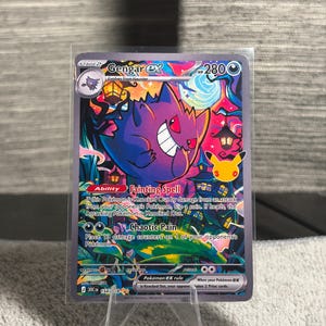 Puede incluir: Una carta coleccionable Gengar ex con 280 HP, que muestra un personaje de tipo fantasma morado en una escena nocturna vibrante y colorida con luna llena, linternas y árboles oscuros. La carta muestra el texto de la habilidad Fainting Spell y el ataque Chaotic Pain.