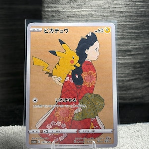 Puede incluir: Una carta coleccionable Pokémon japonesa que muestra a Pikachu sobre la espalda de una persona con un kimono rojo de flores y un obi verde. La carta muestra el nombre Pikachu en japonés, 60 HP y el texto 227/S-P, 2021 Pokémon, Creatures, GAME FREAK.