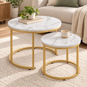 May include: A set of two round nesting tables featuring white faux marble tops with grey veining and gold-colored metal frames. The larger table holds a potted green plant on a book, while the smaller table holds a beige ceramic mug.