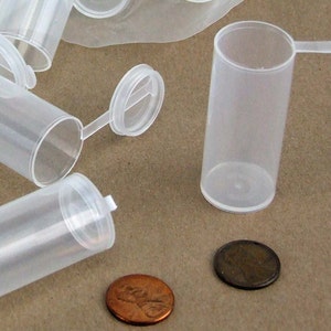 May include: A group of clear plastic vials with hinged lids. The vials are approximately 2.5 cm in diameter and 5 cm tall. The vials are sitting on a brown surface.