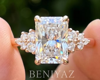 Puede incluir: Un anillo de oro rosa con una gran piedra central rectangular de corte radiante, flanqueada por un grupo de tres piedras redondas de corte brillante a cada lado. El texto BENIYAZ LAB GROWN está impreso en blanco bajo la montura.