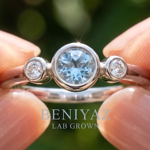 Blue gemstone three stone bezel ring with natural diamond side stones in polished rose gold.