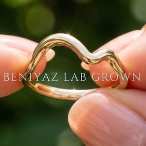 Curved V shaped wedding band in 14K yellow gold, plain chevron contour ring held between fingertips