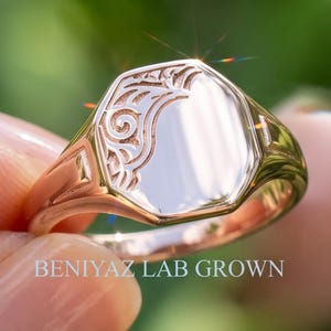 Personalized oval signet ring held by hand with polished engraving face, vintage floral scrollwork shoulders and tapered shank