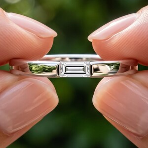 Hand held baguette lab grown diamond wedding band showing the horizontal bar set stone and slim polished gold shank.