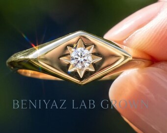 Puede incluir: Un anillo de oro con un engaste en forma de marquesa y un grabado central de estrella que sostiene un diamante redondo de talla brillante. La banda es lisa y pulida. El texto BENIYAZ LAB GROWN es visible en la superficie del anillo.