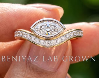May include: A gold ring featuring a central marquise-cut stone in a bezel setting, accented by a curved band set with small round stones. The text BENIYAZ LAB GROWN is visible on the ring. The design combines a polished gold finish with clear stones.