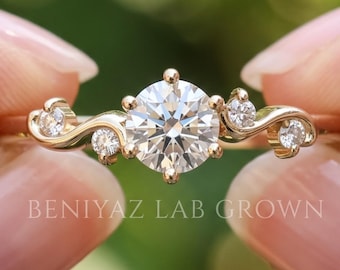 Puede incluir: Un anillo de oro con una gran piedra central redonda de talla brillante, flanqueada por dos piedras redondas más pequeñas a cada lado en una banda de metal curva. El texto BENIYAZ LAB GROWN es visible en el anillo. Incluye cuatro piedras.