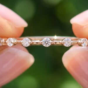 May include: A thin rose gold band ring featuring a series of evenly spaced, round, brilliant-cut white stones set in a delicate metal frame. The text BENIYAZ LAB GROWN is printed at the bottom of the image in a simple, clean font.