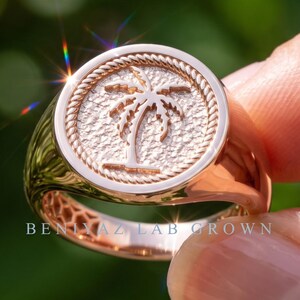 May include: A rose gold signet ring featuring a circular face with a textured background and a raised palm tree emblem. The circular face is bordered by a rope-style design. The text BENIYAZ LAB GROWN is visible on the lower band of the ring.