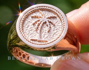 May include: A rose gold signet ring featuring a circular face with a textured background and a raised palm tree emblem. The circular face is bordered by a rope-style design. The text BENIYAZ LAB GROWN is visible on the lower band of the ring.