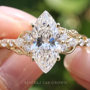 May include: A gold ring featuring a large marquise-cut center stone flanked by smaller round and marquise-cut accent stones on a decorative band. The text BENIYAZ LAB GROWN is visible at the bottom of the image.