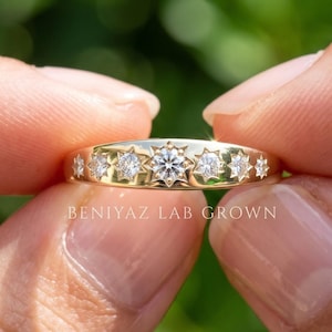 May include: A gold band ring featuring seven flush-set round brilliant cut stones arranged in a row. Each stone is surrounded by a star-shaped engraving. The text BENIYAZ LAB GROWN is printed in white below the ring on the image.