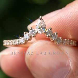 Hand holding a curved lab grown diamond wedding band in 14K yellow gold with pear and round diamonds, 0.30 CT TW chevron nesting ring design