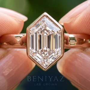 Bezel engagement ring with an elongated hexagon step cut lab grown diamond solitaire on a plain gold band