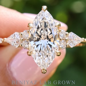 May include: A gold ring featuring a large marquise-cut center stone flanked by two pear-cut side stones and smaller round accent stones. The band is thin and metallic. The text BENIYAZ LAB GROWN is visible at the bottom of the image.