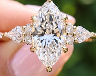 May include: A gold ring featuring a large marquise-cut center stone flanked by two pear-cut side stones and smaller round accent stones. The band is thin and metallic. The text BENIYAZ LAB GROWN is visible at the bottom of the image.