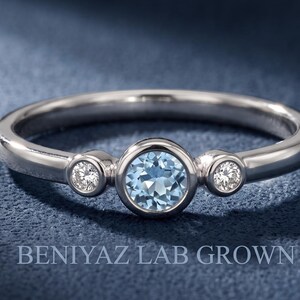Three stone blue gemstone ring with two bezel set natural diamond accents on a slim polished yellow gold band.