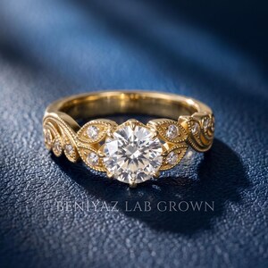 Yellow gold vintage engagement ring featuring a round lab grown diamond center stone, decorative leaf motifs, milgrain detailing and sparkling side diamonds in a floral inspired design.