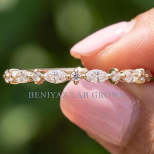 May include: A gold band ring featuring a series of alternating marquise-cut and round-cut white stones set in a horizontal row. The text BENIYAZ LAB GROWN is printed in light blue letters across the center of the ring band.