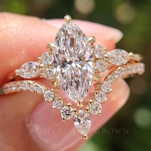 May include: A gold ring set featuring a large marquise-cut center stone surrounded by smaller round and marquise-cut stones, paired with a curved band encrusted with round stones. The text BENIYAZ LAB GROWN is visible at the base.