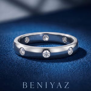 May include: A polished silver-toned band ring featuring multiple round, clear, bezel-set stones embedded along the outer circumference. The text BENIYAZ LAB GROWN is printed in white at the bottom of the image, centered below the ring.