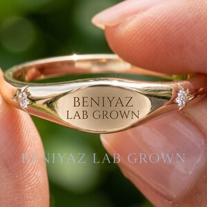 Hand holding a personalized gold wedding band with custom BENIYAZ engraving, polished finish and minimalist ring design against a natural green background