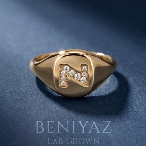 Custom initial N diamond signet ring in solid 14K yellow gold, featuring sparkling lab grown diamonds set into the letter N, photographed on a luxury deep blue background.