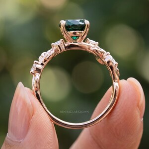 Back profile of botanical emerald ring showing open prong basket, slim shank and decorative leaf shoulders.