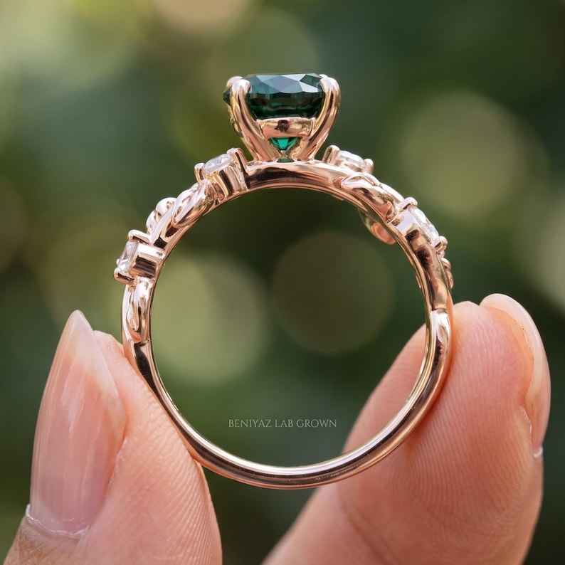 Back profile of botanical emerald ring showing open prong basket, slim shank and decorative leaf shoulders.