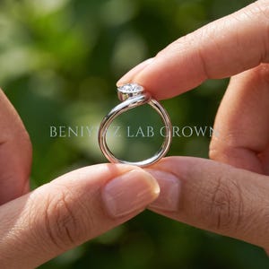Side profile of a sculptural pear diamond bypass ring showing the curved teardrop-shaped shank and polished metal finish.