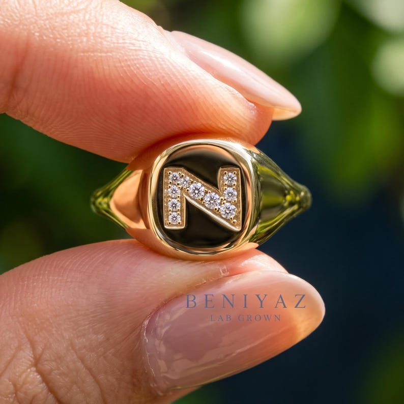 Close up hand view of personalized initial ring in yellow gold with lab grown diamond details and bold modern signet style