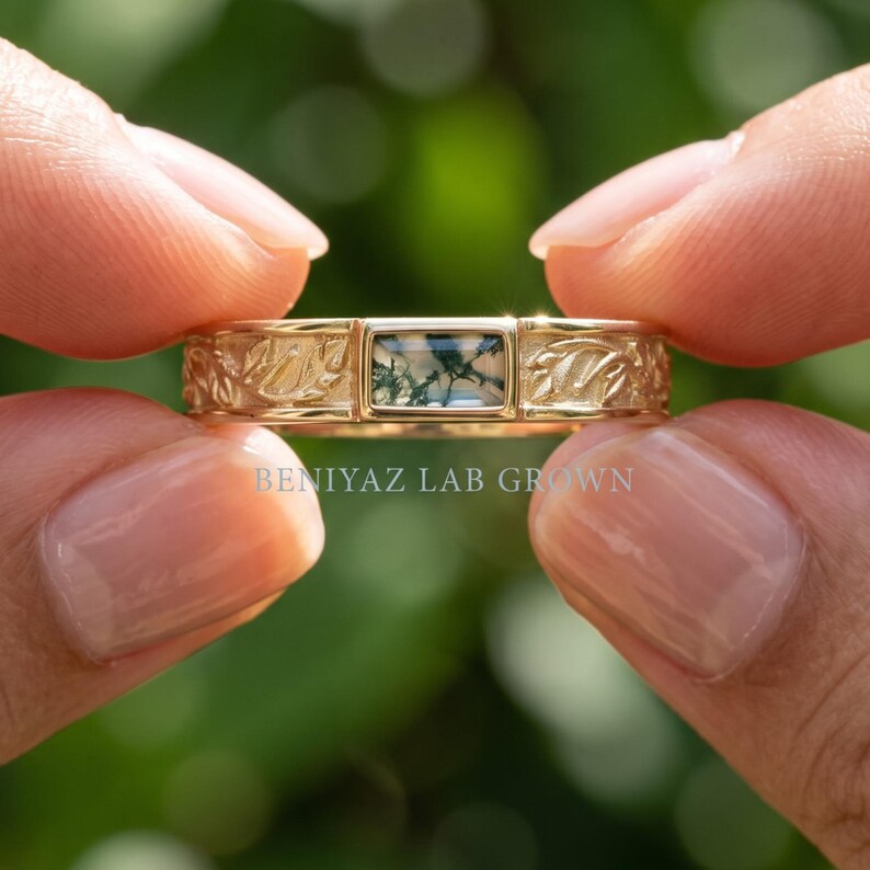 Puede incluir: Un anillo de oro con una piedra de &aacute;gata musgosa rectangular con inclusiones verdes. La banda est&aacute; decorada con un patr&oacute;n de hojas en relieve a ambos lados de la piedra central. El texto BENIYAZ LAB GROWN est&aacute; impreso en blanco en el anillo.