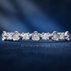 May include: A silver-toned ring featuring an alternating pattern of round brilliant-cut stones and five-petaled flower motifs. The band is engraved with the text BENIYAZ LAB GROWN. The design consists of clear, sparkling stones set in metal.