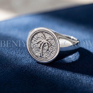 Sterling silver palm tree signet ring with round medallion face, textured palm motif, rope-style border and smooth tapered polished band