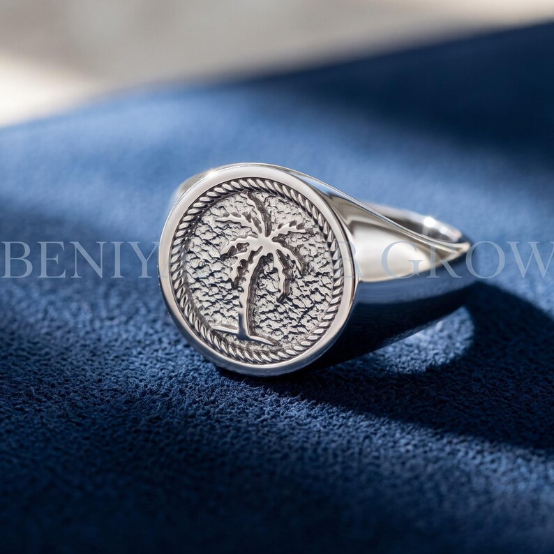 Sterling silver palm tree signet ring with round medallion face, textured palm motif, rope-style border and smooth tapered polished band