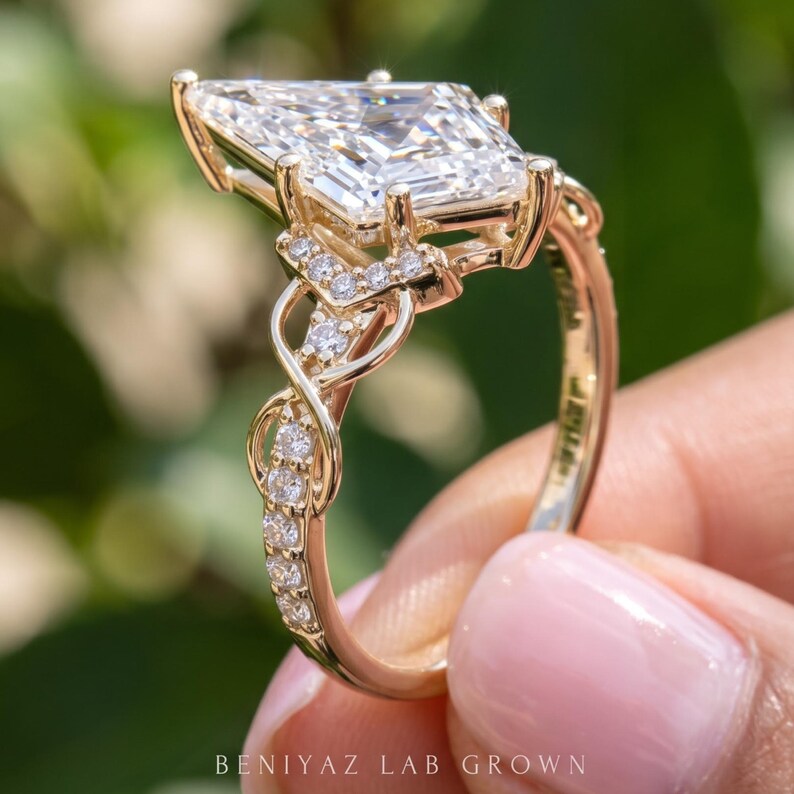 Full side view of a kite cut lab grown diamond engagement ring held upright between fingertips. The photograph displays the raised gemstone setting, decorative gallery and infinity style pavé shoulders extending down the slender gold tone shank.