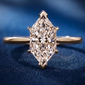 Op de afbeelding: Een ros&eacute;gouden ring met een in marquise geslepen middensteen met een gefacetteerd oppervlak, vastgehouden door zes pootjes. De ringband is glad en gepolijst. De tekst BENIYAZ LAB GROWN is zichtbaar aan de basis van de steen op het blauwe oppervlak.