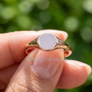 Minimalist round signet ring held at an angle showing smooth blank face, tapered shoulders and clean high polish design