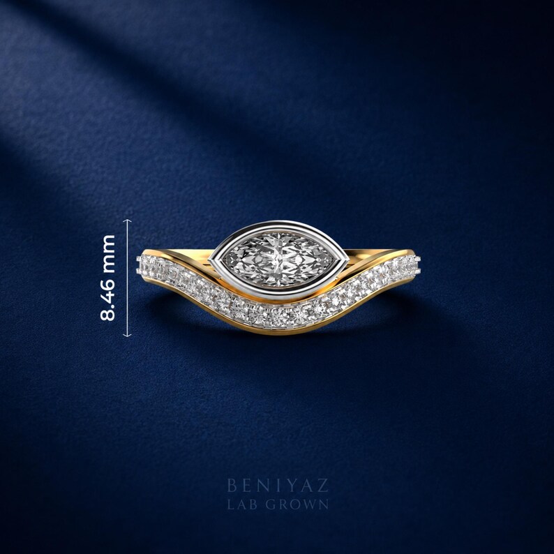 Two tone marquise lab grown diamond engagement ring featuring a bezel set center stone with curved pave diamond wedding band on luxury blue background.